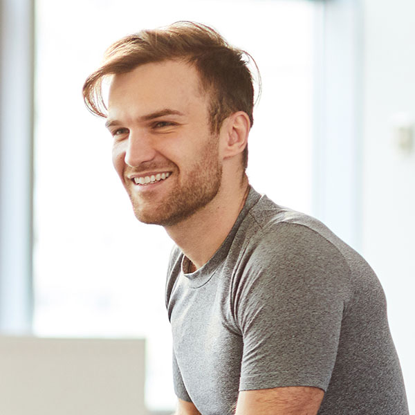 Group of positive curious young students sitting on floor in room full of natural light and talking to yoga teacher at seminar